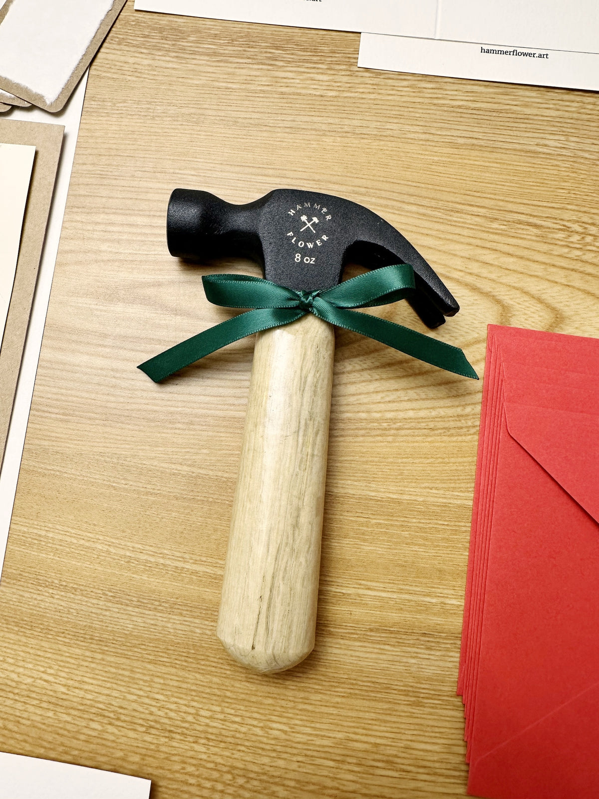 Compact HammerFlower steel hammer with a wooden handle and green ribbon beside red envelopes